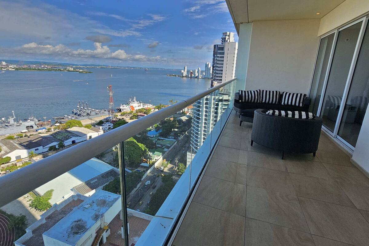 A balcony with a view of a body of water, a ship, and distant buildings.