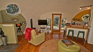 Un soggiorno accogliente con pavimento in legno, una finestra tonda, una televisione e un'area pranzo con sgabelli e un bancone bar.