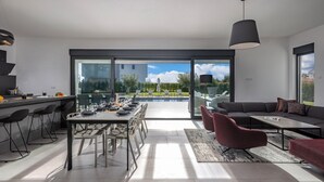 A modern kitchen with a dining area, large sliding glass doors leading to a pool, and a seating area with a sofa and chairs.