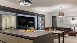 A modern kitchen with a large island, dining area, and a living space with a sofa and a lamp.
