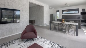 A modern kitchen with a dining area, a flat-screen TV mounted on the wall, and a red chair in the living space.