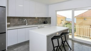 A modern kitchen with white cabinets, a marble backsplash, and a view of the sea through large windows. - 2-Bedroom Holiday Apartment with Sea-view Balcony! (Orebic)