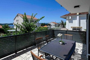 A balcony with a table and chairs, a potted plant, and a view of houses and the sea.
