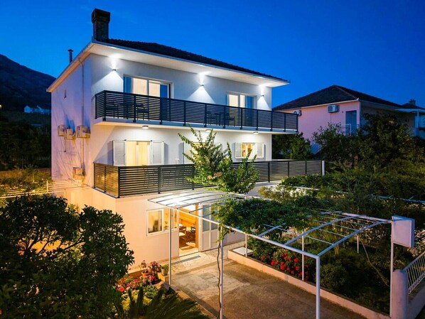 A modern two-story house with a balcony, a covered patio, and a well-maintained garden.