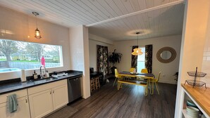 Een moderne keuken met witte kasten, een zwart aanrecht en een houten eettafel met gele stoelen.