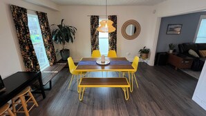 Een eethoek met een houten tafel en gele stoelen, een potplant en een hanglamp.