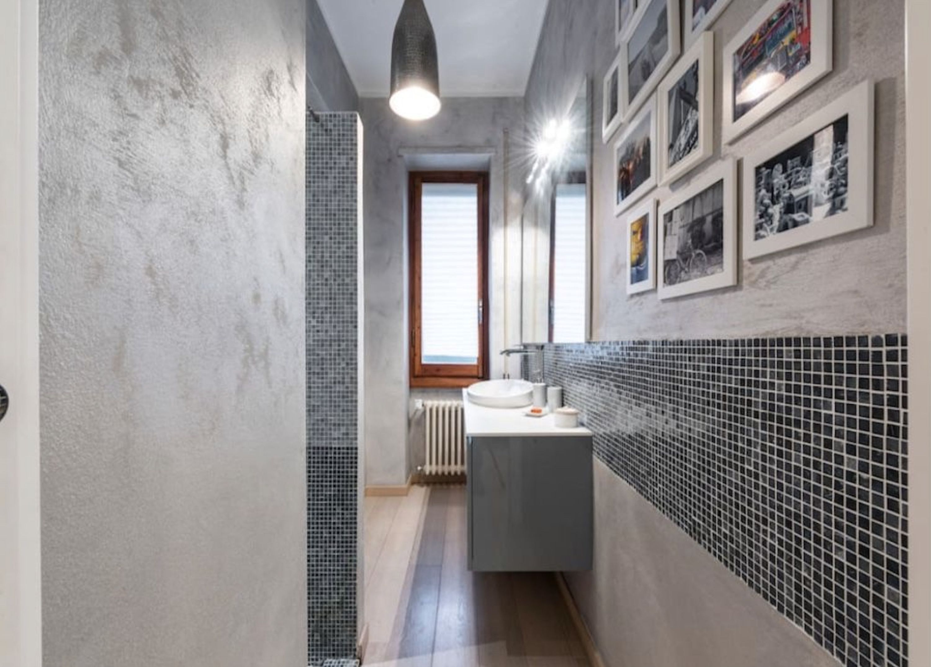 Une petite salle de bain avec un mur recouvert de carreaux, un lavabo et une fenêtre avec des stores.