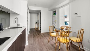 A modern kitchen with white cabinetry, a stainless steel sink, and a built-in oven. There is a dining area with a round table and four gold chairs. The floor is wooden, and the walls are white. - GLOBALSTAY 1 Bedroom with a Romantic View of Trains in Downtown (Toronto/Canada)