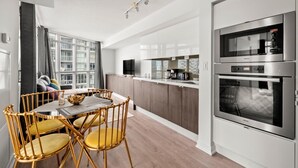 A modern kitchen with a dining area, featuring a large window, stainless steel appliances, and a wooden dining table with chairs. - GLOBALSTAY 1 Bedroom with a Romantic View of Trains in Downtown (Toronto/Canada)