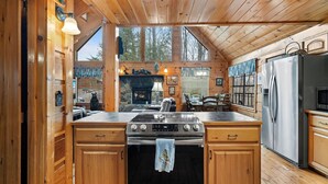 A wooden cabin kitchen with a stone fireplace, stainless steel appliances, and large windows.