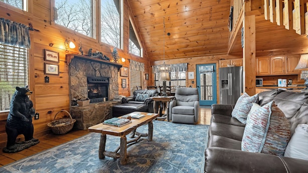 A cozy cabin interior with a stone fireplace, leather furniture, and large windows.
