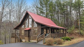 A wooden cabin with a red roof, a porch, and a staircase leading to the entrance.