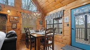 A wooden cabin interior with a dining table, chairs, a chandelier, and a blue door.