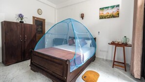 A bedroom with a bed under a mosquito net, a wooden wardrobe, a small table with a teapot, and a painting on the wall. - 10 mins to Surf Point! Newly Renovated Air-Conditioned Balcony Room with WiFi (Matara)