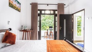 A hotel room with a bed, a wooden table, a small round table with chairs, and a view of greenery outside. - 10 mins to Surf Point! Newly Renovated Air-Conditioned Balcony Room with WiFi (Matara)