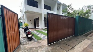 A two-story building with a gated entrance, a paved driveway, and a parked scooter. - 10 mins to Surf Point! Newly Renovated Air-Conditioned Balcony Room with WiFi (Matara)