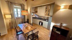 A compact kitchen with modern appliances, a dining area with a wooden table and chairs, and a cozy living space with a bookshelf. - Villa 7 (Bagno A Ripoli)