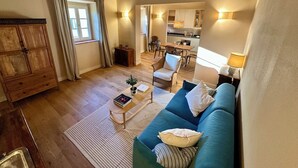 A cozy living room with a sofa, a coffee table, and a wooden cabinet. There is a window with curtains, a kitchen area in the background, and a dining table with chairs. - Villa 7 (Bagno A Ripoli)