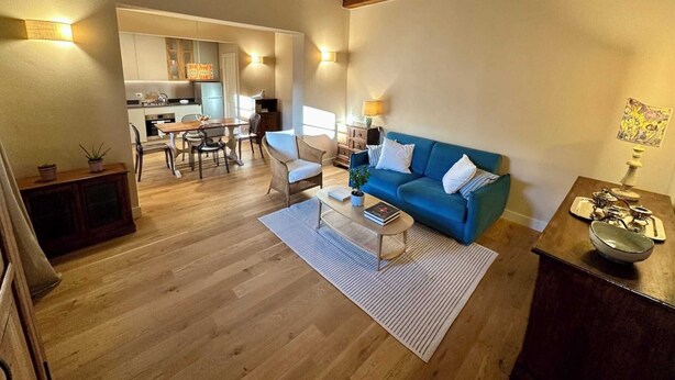 A living room with a blue sofa, wooden flooring, and a dining area with a table and chairs. - Villa 7 (Bagno A Ripoli)