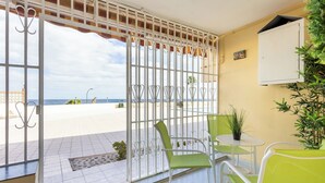 Un balcón con vista a la playa, una pequeña mesa con sillas y una planta en maceta.