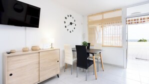 Un comedor moderno con un armario de madera, un reloj negro, un televisor montado en la pared y vistas a través de una puerta de vidrio.