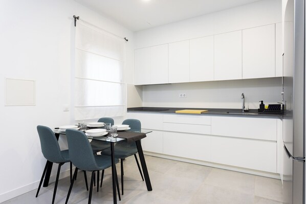 A modern kitchen with white cabinets, a black countertop, and a dining area with a glass table and chairs.