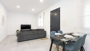 A modern living room with a grey sofa, a TV, and a dining area with a glass table and blue chairs. - Home2Book Modern Apt Indoor Terrace, La Laguna (San Cristóbal de La Laguna)