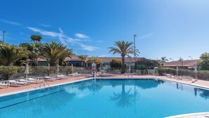 A clear blue pool with lounge chairs and umbrellas, surrounded by palm trees and a fence. - Home2Book Vibrant Maspalomas Stay, Pool & Terrace (Maspalomas)