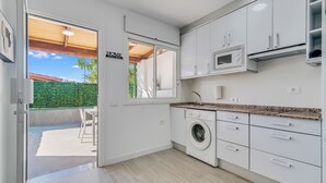 A modern kitchen with white cabinets, a built-in washing machine, and a view of the outdoor patio. - Home2Book Vibrant Maspalomas Stay, Pool & Terrace (Maspalomas)