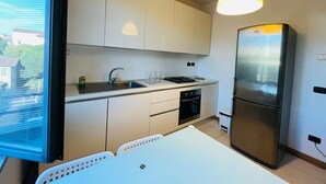 A modern kitchen with white cabinets, a stainless steel refrigerator, a gas stove, and a window overlooking a residential area.