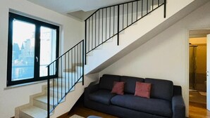 A modern living room with a staircase, a sofa, and a large window.