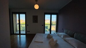 A bedroom with a large bed, two windows, and a view of a building and trees.