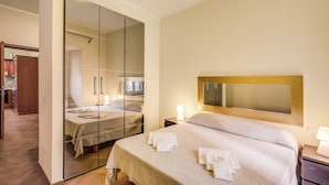 Une chambre d’hôtel avec un grand miroir, un lit avec des serviettes soigneusement pliées, une table de chevet avec une lampe, et une vue sur la salle de bain attenante.