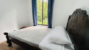 Un letto singolo con una testiera in legno, biancheria da letto bianca e una finestra con tende azzurre.