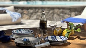 A dining setup with plates, cutlery, and glasses on a wooden table, with a stone wall and a pool in the background. - Evelyn's Pool Garden (Forio)