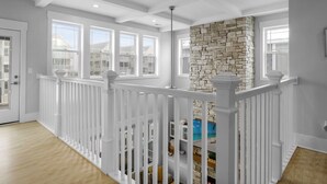 Un balcon spacieux avec des balustrades blanches, un mur d’accent en pierre et de grandes fenêtres offrant une vue sur les bâtiments voisins.