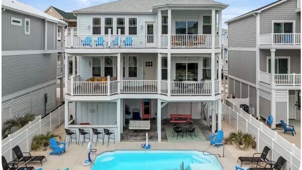 Un immeuble résidentiel à plusieurs étages, doté de balcons, d’une piscine et d’un espace extérieur aménagé pour s’asseoir.