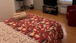 A bedroom with a bed, a TV, a red chair, a wardrobe, and a bathroom visible through an open door. - Charming studio in the heart of Strasbourg (Strasbourg)