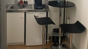 A compact kitchenette with white cabinets, a microwave, a coffee maker, and a small table with stools. - Charming studio in the heart of Strasbourg (Strasbourg)