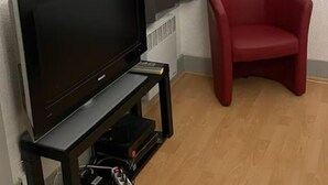 A room with a television on a black stand, a red chair, and a white door with a window. - Charming studio in the heart of Strasbourg (Strasbourg)