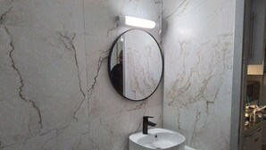 A bathroom with a marble wall, a round mirror, and a white sink with a black faucet. - Charming studio in the heart of Strasbourg (Strasbourg)