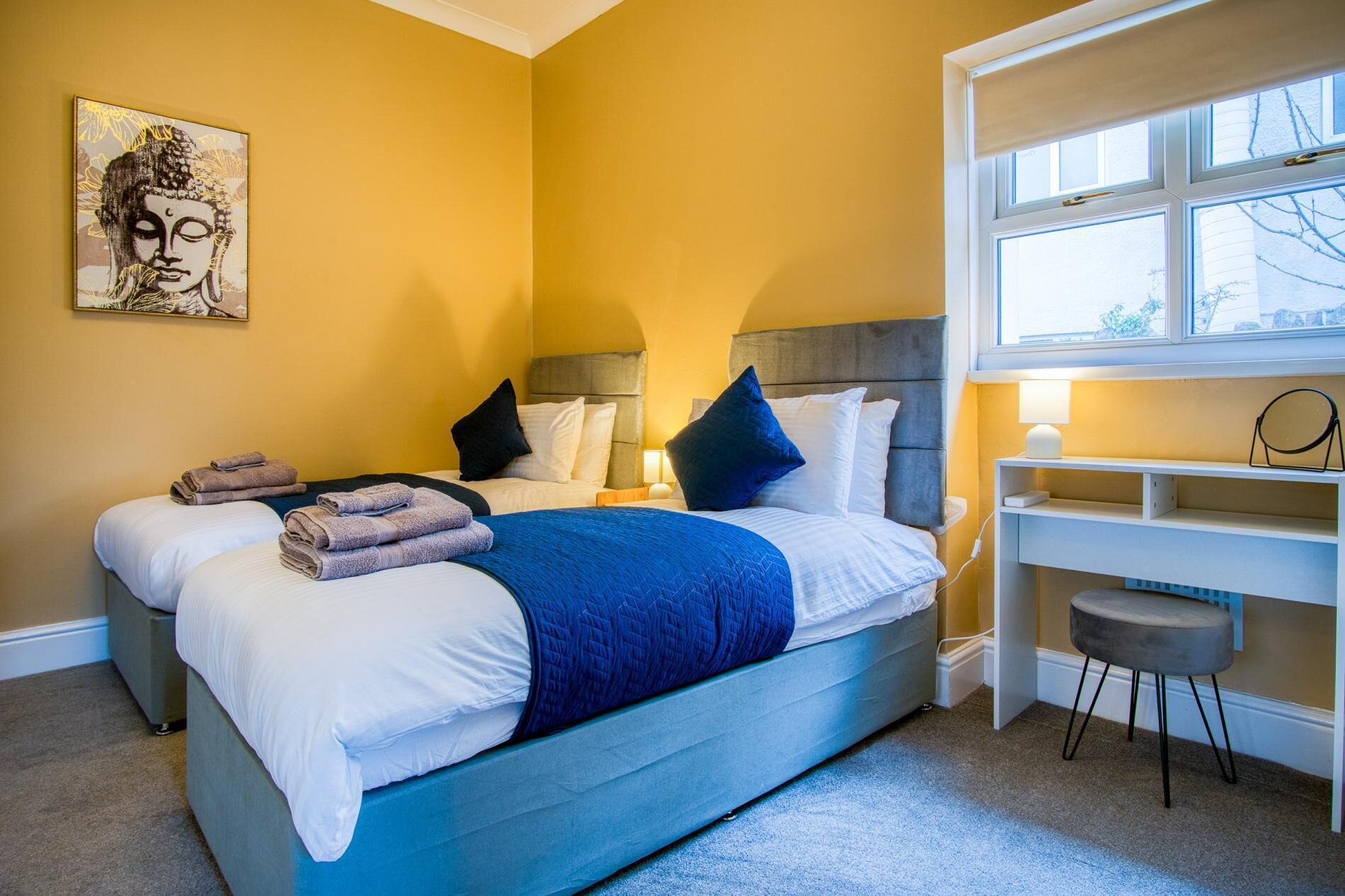 A hotel room with two beds, a desk, and a window.