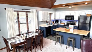 A compact kitchen with white cabinets, a central island, and a dining area with a table and chairs. - TF26-Quaint Cottage! Pets Ok! Fire Pit! (Davis)