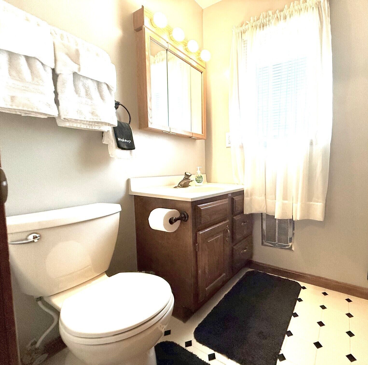 Een badkamer met toilet, wastafel, wastafelmeubel en een spiegel met verlichting erboven.