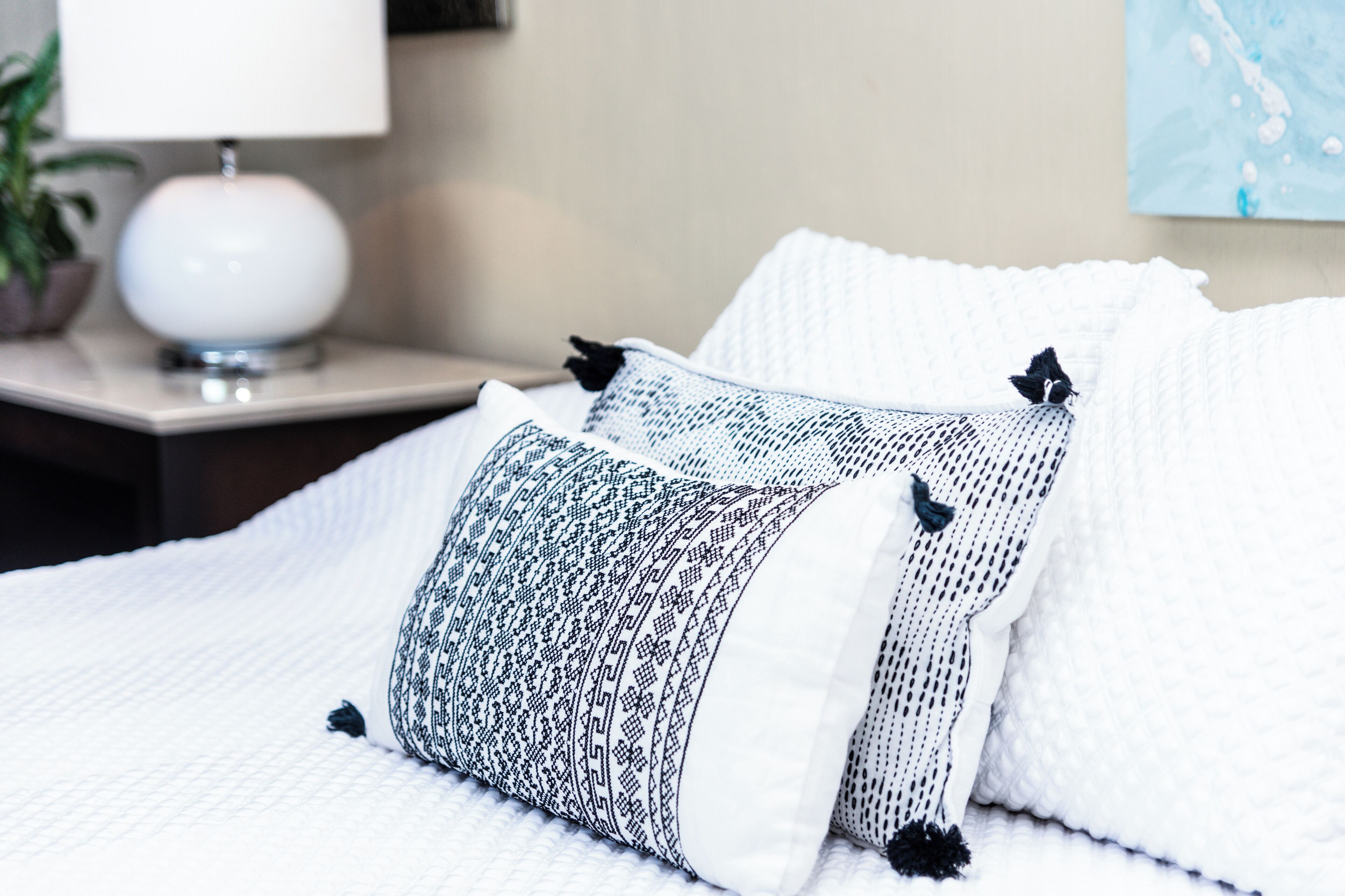 A neatly made bed with patterned pillows and a white lamp on a bedside table.