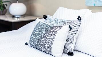 A neatly made bed with patterned pillows and a white lamp on a bedside table.