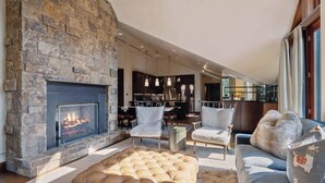 A modern living room with a stone fireplace, leather ottoman, and a sofa with patterned cushions. - Solaris PHHW - 3 Bedroom (Vail)