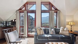 A spacious living room with a large window, a cozy sofa, a chair, and a leather ottoman. - Solaris PHHW - 3 Bedroom (Vail)