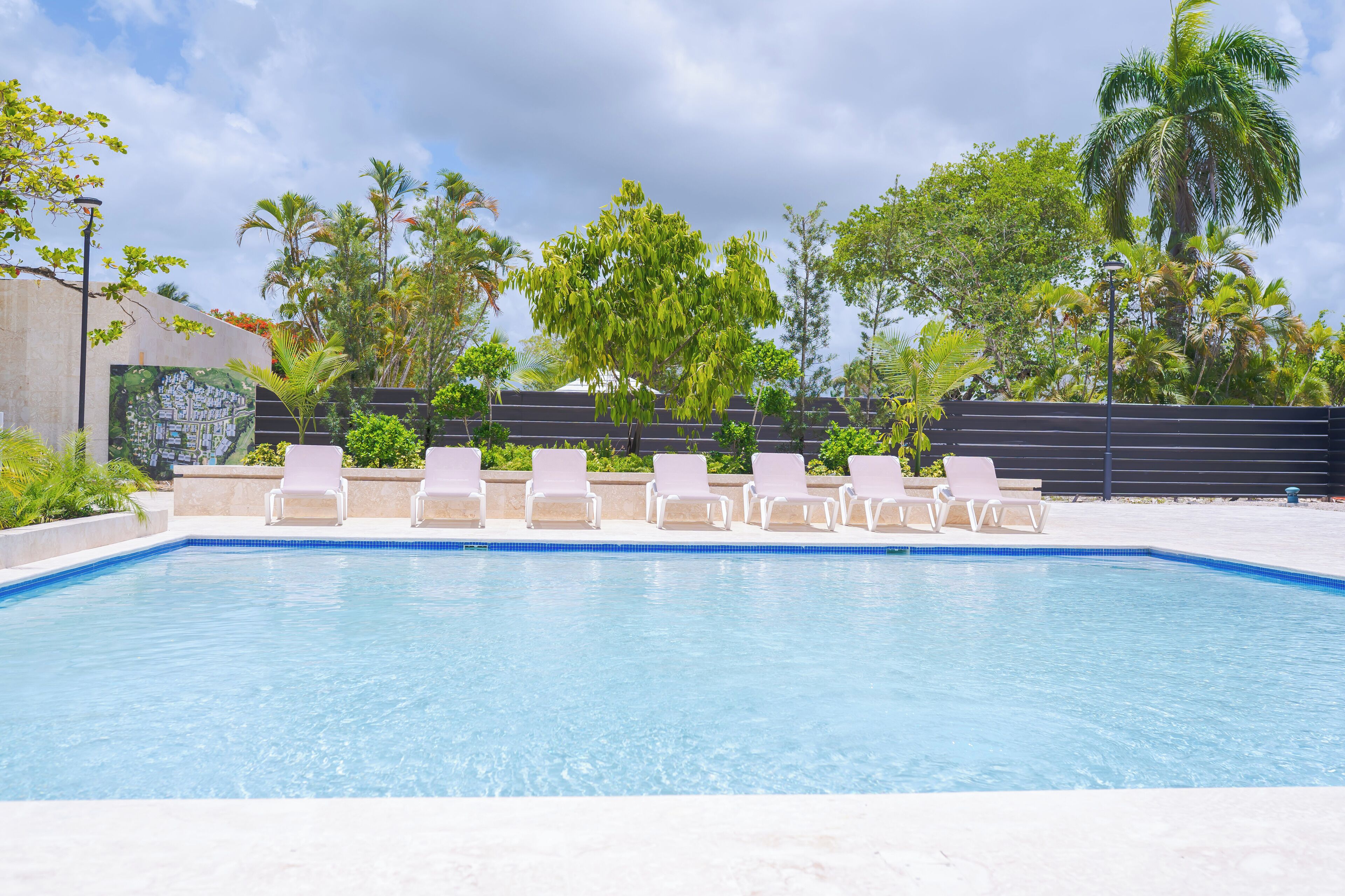 Una piscina con lettini bianchi e vegetazione tropicale sullo sfondo.