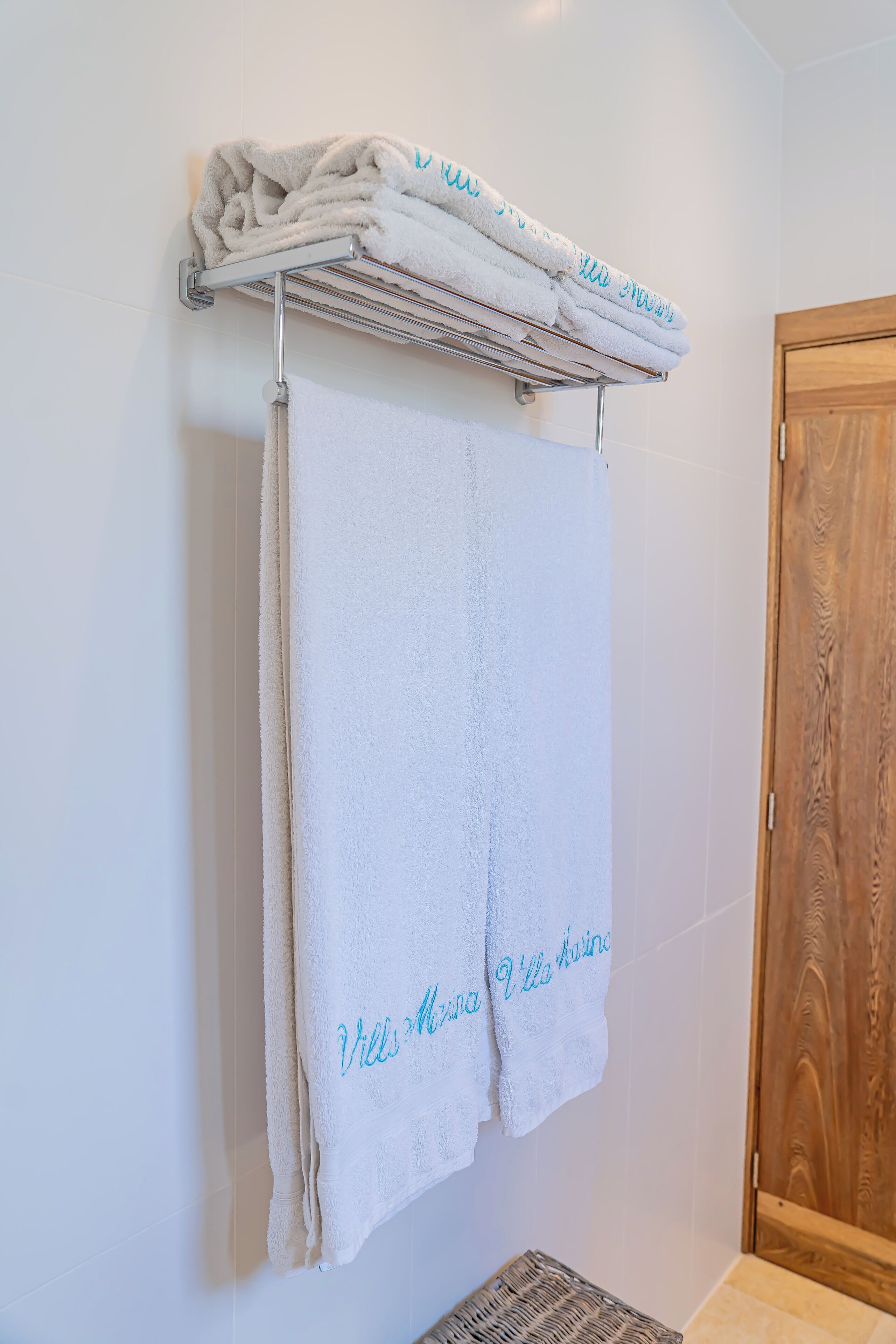A bathroom with a towel rack holding folded towels and a towel with "Villa Maria" written on it.